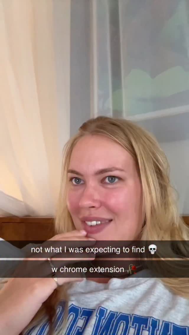 A young woman with blonde hair and blue eyes is shown in a selfie-style shot. She's wearing a gray t-shirt with blue lettering and is smiling slightly. The overlay text reads 'not what I was expecting to find' and 'w chrome extension' along with a skull emoji and a rose emoji. The background is softly lit, with curtains or a sheet visible.
