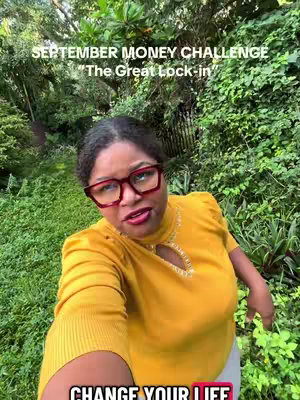 A woman with dark hair and red square glasses poses for a selfie outdoors. She wears a yellow top and is surrounded by green foliage. Text overlays read 'September Money Challenge' and 'The Great Lock-in'.