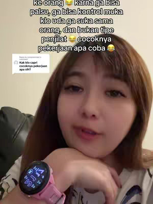 A young woman is centered in the frame, her head and upper body visible. Text overlays are present at the top, while she wears a pink watch. She is looking towards the camera and speaking.