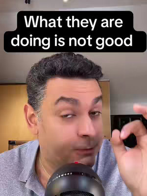 A selfie-style shot featuring a man in a grey shirt in front of a neutral background. He is holding a microphone with one hand and making an okay gesture with the other. Text overlayed at the top reads 'What they are doing is not good'.