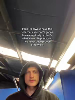 A person wearing a black hooded sweatshirt is centered in the frame. Text is overlaid at the top of the image. The background is dark and contains some metal elements with overhead lighting.