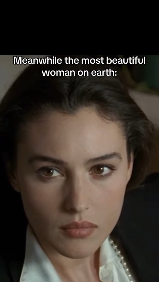 Close-up shot features a woman with dark hair looking directly at the camera. The text overlay reads, "Meanwhile the most beautiful woman on earth:" with the woman identified as Monica Bellucci.
