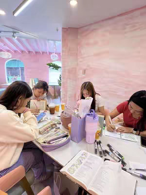 The cover image shows a group of four young women sitting around a table in a brightly lit, pink-themed room. They are engaged in what appears to be a bible study or journaling session, with each person having an open book and writing materials in front of them. Stationary and beverages are also present on the table, suggesting a comfortable and focused atmosphere.