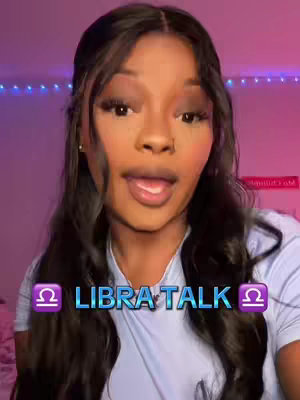 A woman with long dark hair is centered in the frame, slightly off-center. She is looking at the camera and speaking, with her mouth open as if mid-sentence. The background is blurred but appears to be a pink and purple gradient lit with string lights. In the foreground, a text overlay declares LIBRA TALK between two Libra zodiac symbols.