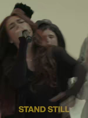 The cover image shows a group of people standing close together, two women are centered, one holding a microphone to her mouth as if singing and another one looks straight ahead with a focused expression. The overall tone of the image is serious, possibly of a performance or religious context.