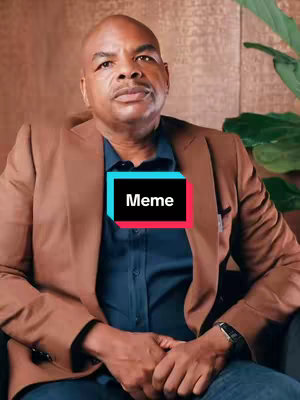 A man wearing a brown blazer and a dark blue shirt sits in front of a brown backdrop of what looks like a wall. A text overlay in a black box with white border and in the center of the image says 'Meme'.