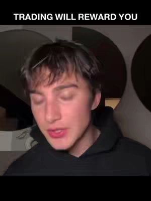 A young man with short brown hair, wearing a black hoodie, is the central figure. He is illuminated by soft lighting, possibly indoors. The background is obscured, featuring large, rounded shapes, potentially decorative elements. The image has a medium shot composition focused on the person's face.