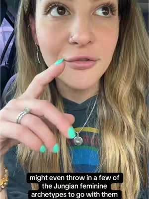 A close-up shot of a woman with long blonde hair, looking towards the upper right of the frame. She is in a car, with a slightly blurred background. She is wearing a dark hoodie and jewelry, including a necklace and a ring with a large stone. Her fingernails are painted a bright turquoise. Below her, a bar of text is visible.