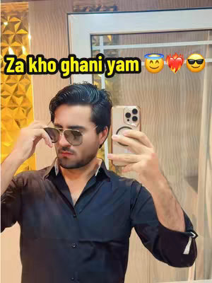A man in a black shirt is taking a mirror selfie. The background includes a gold, textured wall and a glimpse of a door. The man is wearing sunglasses and holding a phone, appearing to be taking the photo. Text overlays with emojis are placed above the man.