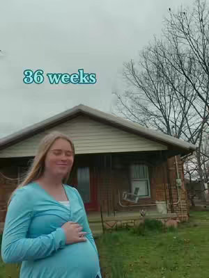 A woman with long blonde hair, wearing a light blue long-sleeved shirt, stands in front of a house. She is visibly pregnant, hand on her belly. The text '36 weeks' is overlaid at the top of the image. The background features a residential house with a porch swing and bare trees.