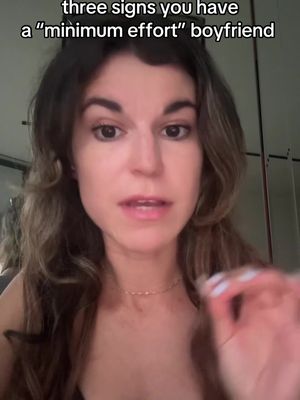 A woman with long brown hair is centered in the frame, talking. The background is blurred. White text overlay at the top reads: "three signs you have a \"minimum effort\" boyfriend."