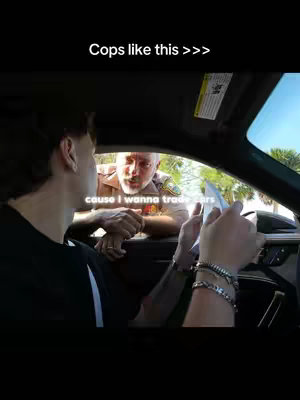 The image shows a scene inside a car. The main subject is a young man in a black shirt looking toward a police officer. The officer is standing outside the car, clearly visible from the chest up, wearing a uniform. A text overlay reads 'Cops like this >>>' at the top of the frame and another overlay says 'cause I wanna trade cars' at the bottom.