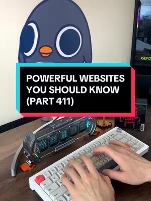 The cover image features a desk setting, with a keyboard at the forefront and a monitor/display behind it. A cartoon penguin-like character is positioned above a black rectangular text overlay that reads, "POWERFUL WEBSITES YOU SHOULD KNOW (PART 411)". The scene is lit with a soft, diffused light, suggesting a studio setting.