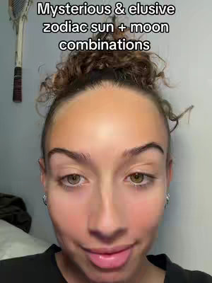 A selfie-style shot featuring a woman with light skin and dark hair styled in a bun. The background appears to be a plain wall. The text overlay reads: "Mysterious & elusive zodiac sun + moon combinations".