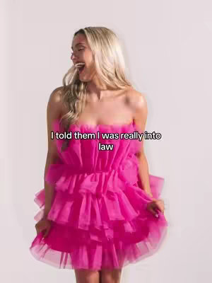 A woman in a pink, strapless dress is laughing and holding the hem of her dress. The background is plain white. Text overlaid on the image reads, 'I told them I was really into law'.
