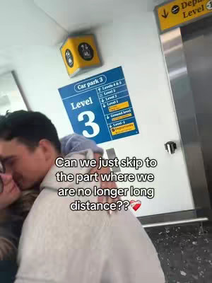 A man hugs someone at an airport departure area. The setting includes airport signage.