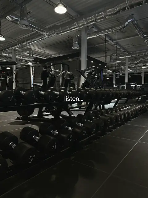 A dimly lit gym interior with rows of dumbbells on racks. The focus is on the equipment, with a text overlay that says listen. The color scheme is dark, with the lighting highlighting the equipment.