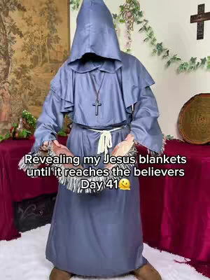 A person in a blue hooded robe is holding open a fringed cloth. The image has a soft, slightly washed-out look, with a background that seems to be composed of two long panels of maroon and a tapestry of a pastoral scene. Text is overlaid on the image in a simple white font, and a digital sun face is present to the right.