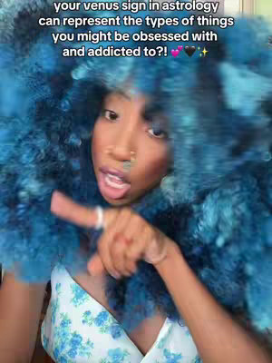 The cover image presents a close-up of a person with blue, voluminous hair styled in a cloud-like manner. The individual, who appears to be a young woman with dark skin, is positioned slightly off-center, looking towards the viewer. She has a nose ring and is making a gesture with her right index finger, which has a silver ring on it. A floral-patterned white top peeks out. The image has a slightly blurred, dreamy aesthetic, and text overlays the top part, set against a dark background.