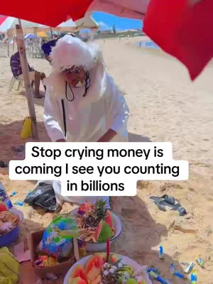 A person in a white outfit and a puffy white hat on a beach. Text over the image reads, 'Stop crying money is coming I see you counting in billions.' Dishes of fruit are on an orange blanket on the sand. The background has umbrellas and people in the distance.