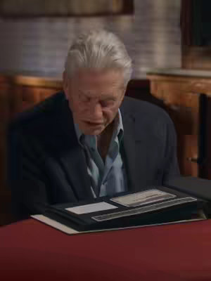 The cover image features Michael Douglas with gray hair, looking down at a photo album on a red-clothed table. He wears a dark blazer over a light blue shirt. The background appears to be an interior with bookshelves.