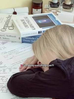 A woman with blonde hair rests her head on a desk covered in textbooks and papers. The books are in German. The overall composition is focused and academic in setting. Text overlay is used, with a quote about studying.