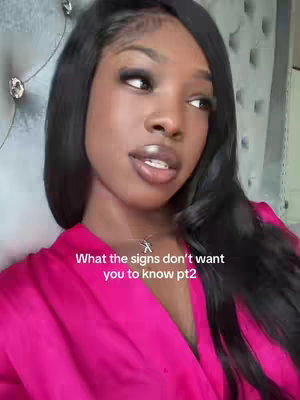 A woman with long black hair and a pink robe is looking slightly to the side with gentle expression. Text overlay states, 'What the signs don't want you to know pt2'. The background is soft with patterned texture, indicating a bedroom setting, and the lighting appears natural or soft.