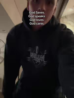 A person wearing a black hoodie is centered in the frame. Overlayed on the image is text in a vertical column. The background appears to be indoors, with hints of a door frame and a light fixture. The lighting is soft, emphasizing the subject.