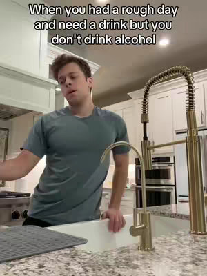 A person stands in a kitchen, near a sink and faucet, looking upwards with a slightly frustrated expression, suggesting a desire for a drink. Text overlay with a white font is at the top, and the background shows a clean, modern kitchen.