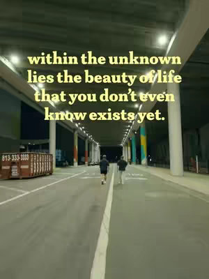 An outdoor shot features a wide, long, concrete road beneath a bridge or overpass, lit with evenly spaced overhead lights. In the distance, two people are walking away from the camera. Overlay text in a soft yellow shade is centered above the heads of the figures, delivering a motivational quote.