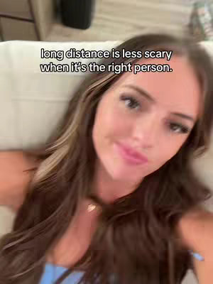 A selfie-style video cover featuring a smiling woman with long, wavy brown hair. She's positioned close enough to the camera that her face dominates the frame. The overlay text reads messages about long distance relationships.