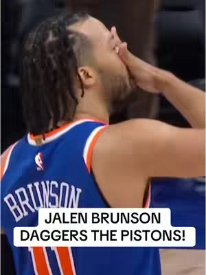 Image shows Jalen Brunson in a basketball jersey, partially obscuring his face with his hand. The text overlay, in a white box at the bottom, reads "JALEN BRUNSON DAGGERS THE PISTONS!". The jersey is blue and orange. The overall composition looks to be a candid moment captured during a game.