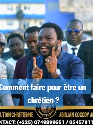 A group of men in a well-lit outdoor setting. The central figure, a Black man with a beard, is wearing a blue shirt and gesturing with his index fingers raised. A text overlay on the bottom portion of the image includes the question, 'Comment faire pour être un chrétien ?' (How to be a Christian?). The background includes several other men and a building, with a logo at the bottom that depicts a lion with the name of the organization.