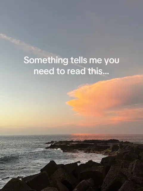 The image showcases a beautiful sunset over the ocean. The sky transitions from a deep blue at the top to shades of pink and orange near the horizon, where fluffy clouds are illuminated by the setting sun. The ocean appears calm, with gentle waves lapping against a rocky shoreline in the foreground. Large, dark, angular rocks form a barrier in the lower portion of the image, providing contrast to the softness of the sky and water. Text in a white, simple font is overlaid on the image.