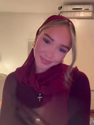 The cover image presents a young woman facing the camera, slightly angled to the side. She is wearing a dark red head covering. A silver cross hangs from a necklace. The background has a warm, soft lighting.