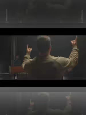 The cover image shows a dark stage setting with a man from the back, raising his arms with his index and pinky fingers extended, creating a 'rock on' gesture. Stage lights are visible behind him with more figures and a keyboard. The overall composition has a dark, atmospheric feel.
