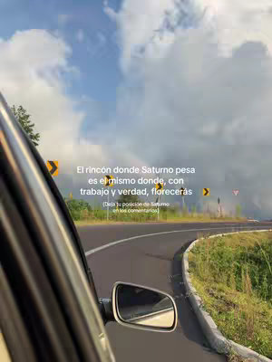The image captures a road winding through a landscape under a cloudy but partially blue sky, viewed from inside a car with part of the car visible on the left side. Text overlays are placed near the right edge, in front of the road signs.