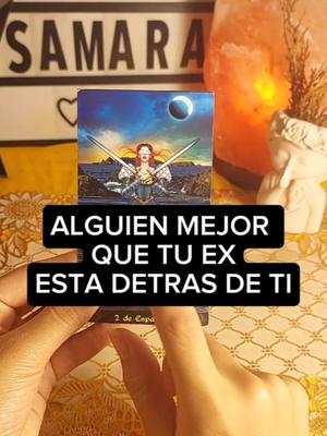 The image shows a tarot card in the hands of someone. The card depicts a woman holding two swords with a dark, ominous sky in the background. Text overlays on the card reads, "ALGUIEN MEJOR QUE TU EX ESTA DETRAS DE TI."