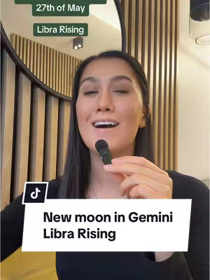 A woman with dark hair, holding a microphone, speaks with a background of wooden slats and a mirror. A graphic in the lower left with white text on a black background says "New moon in Gemini Libra Rising". Overlaid at the top are two green text boxes. One says "27th of May" and another says "Libra Rising".
