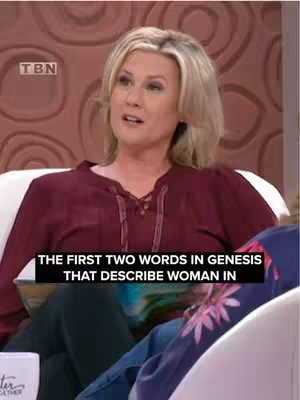 A woman with blonde hair is seated and talking. Above her, a black bar provides text. The background shows a blurred-out room with neutral colors.