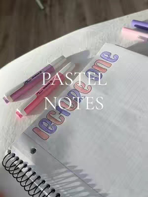 A top-down shot of a notebook with colorful, handwritten text. Two pastel-colored highlighters lie horizontally above the notebook. The top surface appears to be a clean, bright white.