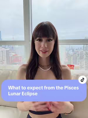 A young woman with long dark hair and a pearl necklace sits in front of a window with a city view. A text overlay reads: "What to expect from the Pisces Lunar Eclipse".