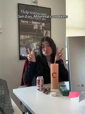 A woman is seated at a white desk, making a peace sign with both hands. She is puckering her lips. On the desk are items including a cup, soda can, and a sign on the wall behind her says, "Help restaurants. Gen Z vs Millennial coworkers", which refers to the conflict between Gen Z and millennial coworkers, implying generational differences in job-related behaviours.