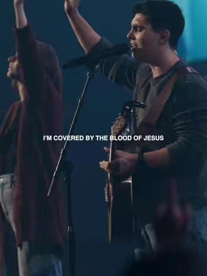 The cover image shows a live performance with a male vocalist in the foreground playing a guitar and singing into a microphone, and another person with arms raised in worship in the background. The stage is softly lit with cool blue and purple hues, and the text overlayed in white text.