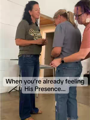 The cover image shows three people, two women and a man. The primary woman in the video is standing with arms at her side, dressed in a short-sleeved olive green t-shirt and blue jeans. One of the other women is bowing her head, and the man is on the right side with his hands near the woman's back.