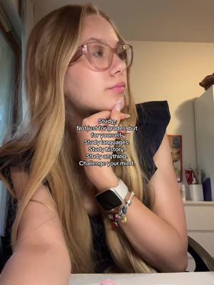 A young woman with long blonde hair and glasses is looking up and to the side. She is wearing a black top and a smartwatch. Text is overlaid on the image.