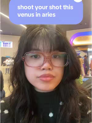 A woman with dark hair and glasses is centered in the frame, looking towards the viewer. A blue speech bubble is above the woman's head with white text.