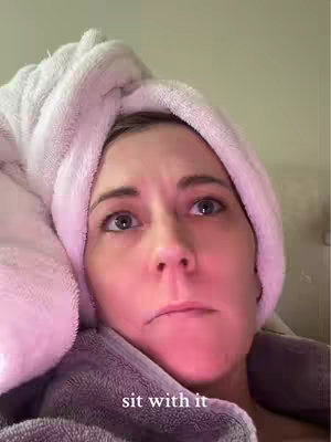 A close-up shot of a woman with light skin wearing a fluffy, white towel turban. She has a slightly concerned expression, looking upwards. The background is a blurry, neutral color.