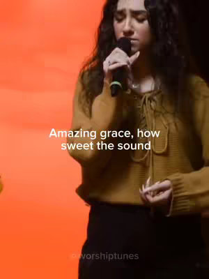 A young woman with long, dark, curly hair sings into a microphone against an orange backdrop. Text overlays the image, repeating the phrase "Amazing grace, how sweet the sound".