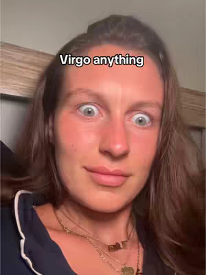 A close-up of a woman with fair skin and light brown hair, set against a neutral background. Her eyes are wide and looking up, with a slight smile playing on her lips. She's wearing a dark blue top and multiple necklaces. A text overlay at the top reads 'Virgo anything'.